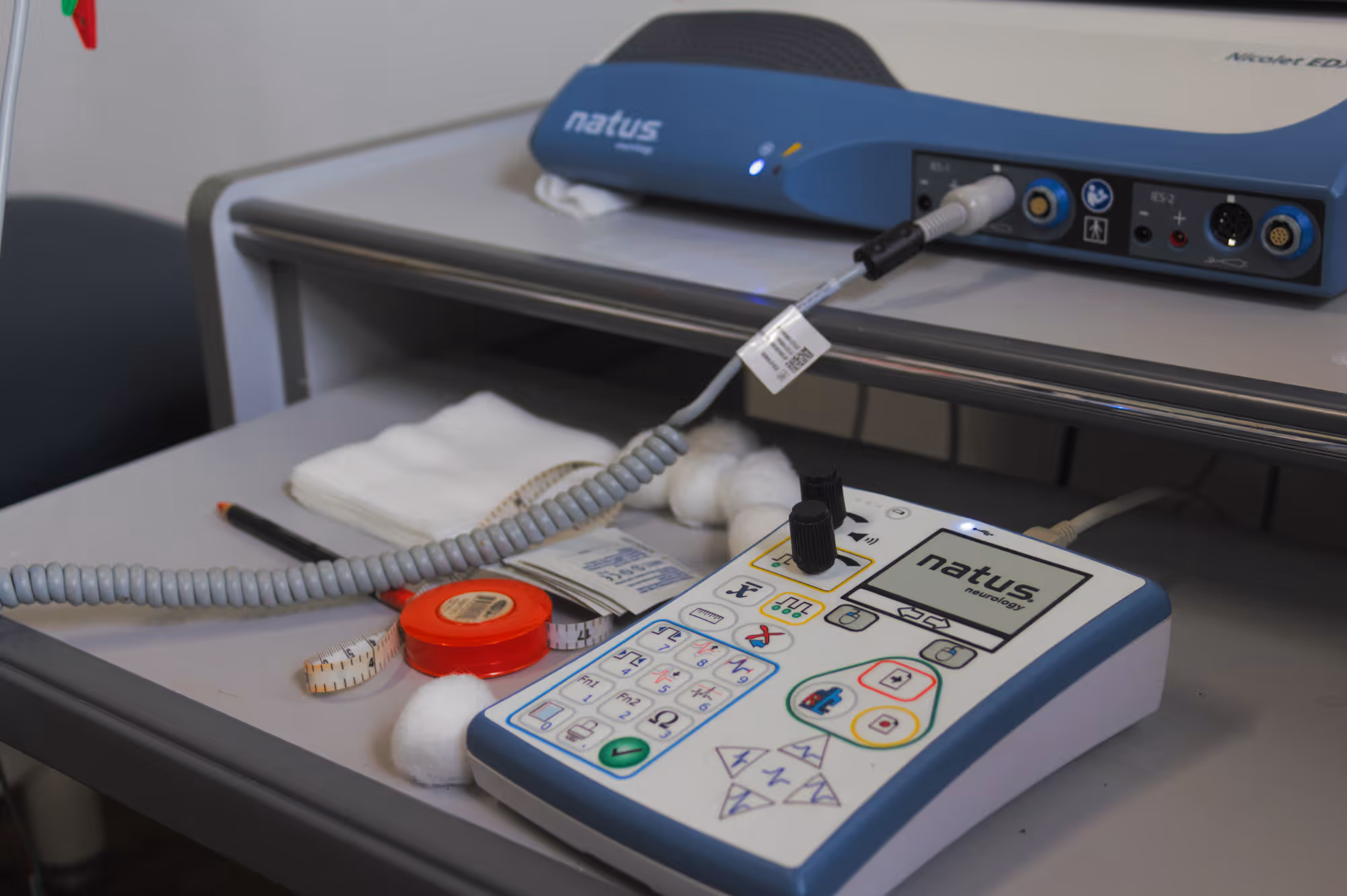 Natus neurology device with buttons and dials on a medical cart surrounded by cotton and measuring tape.