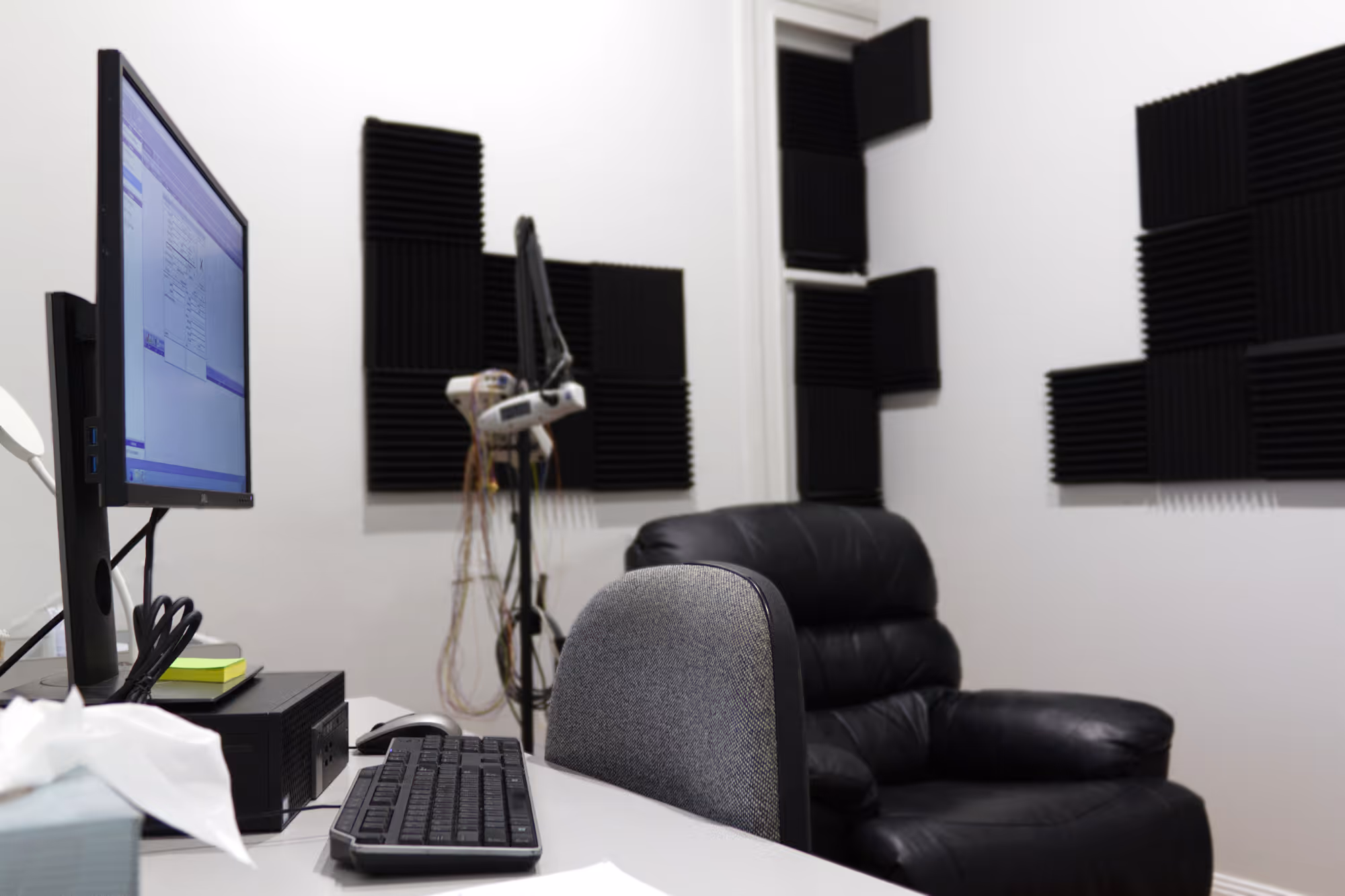 Small room with computer setup, black soundproof foam panels, and a black leather recliner chair.