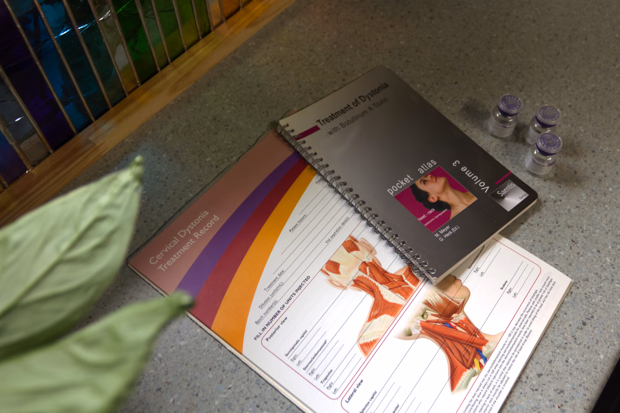 Open medical book showing cervical dystonia muscle treatment with three vials on the side.