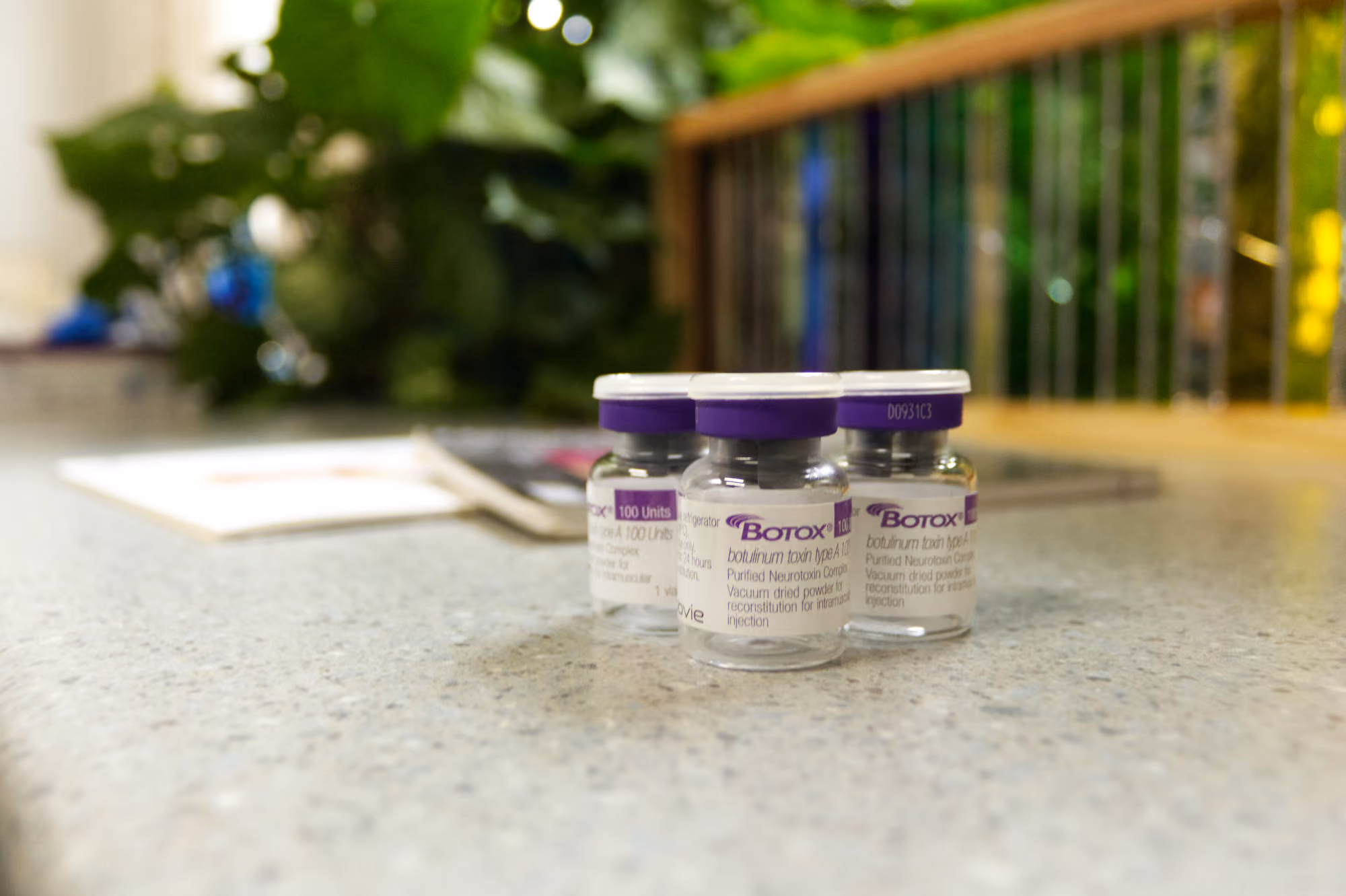 Three small Botox vials with purple caps on a countertop in a medical setting.