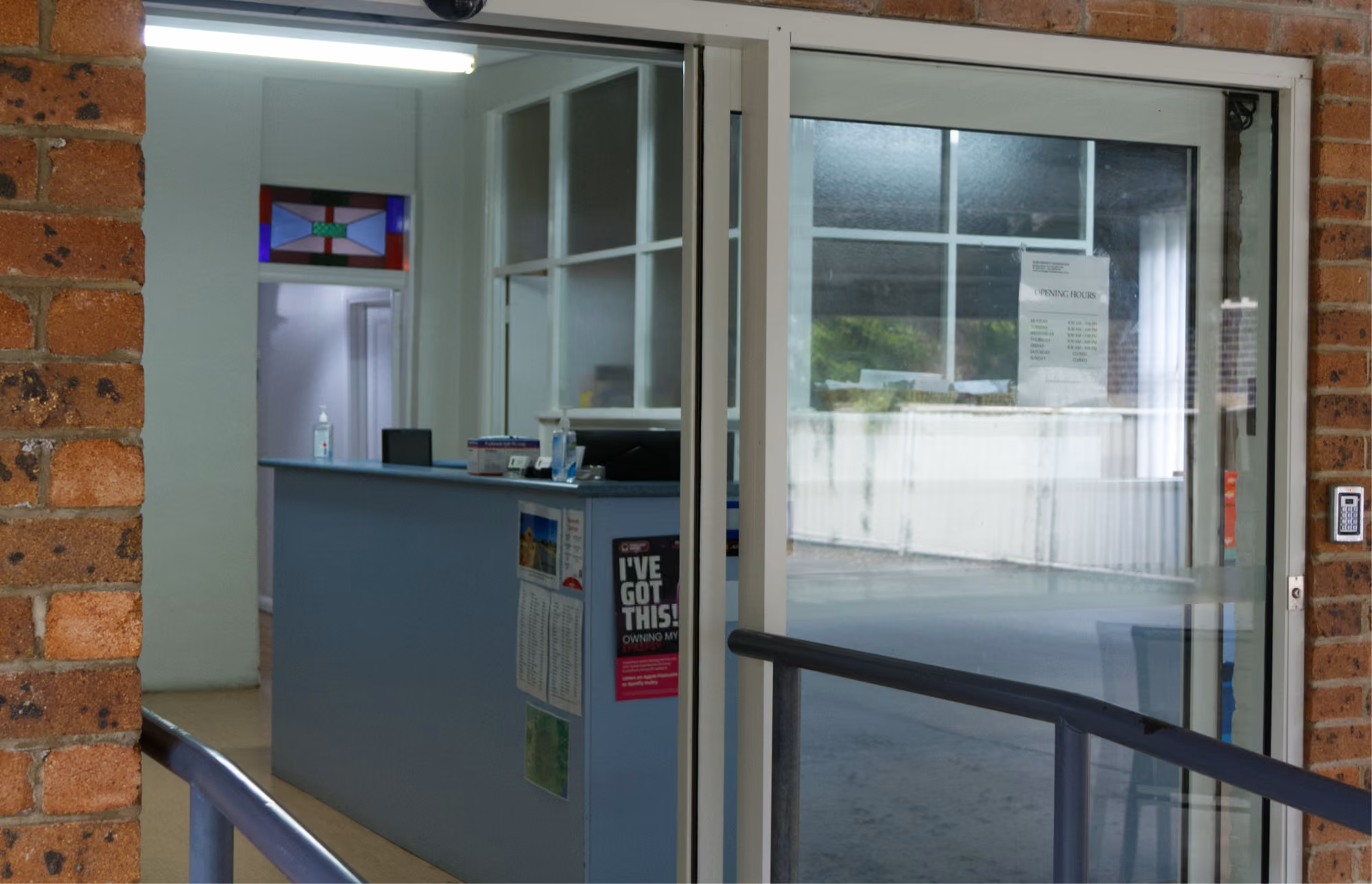 Reception area with blue counter, hand sanitizer, and glass sliding door with keypad access.