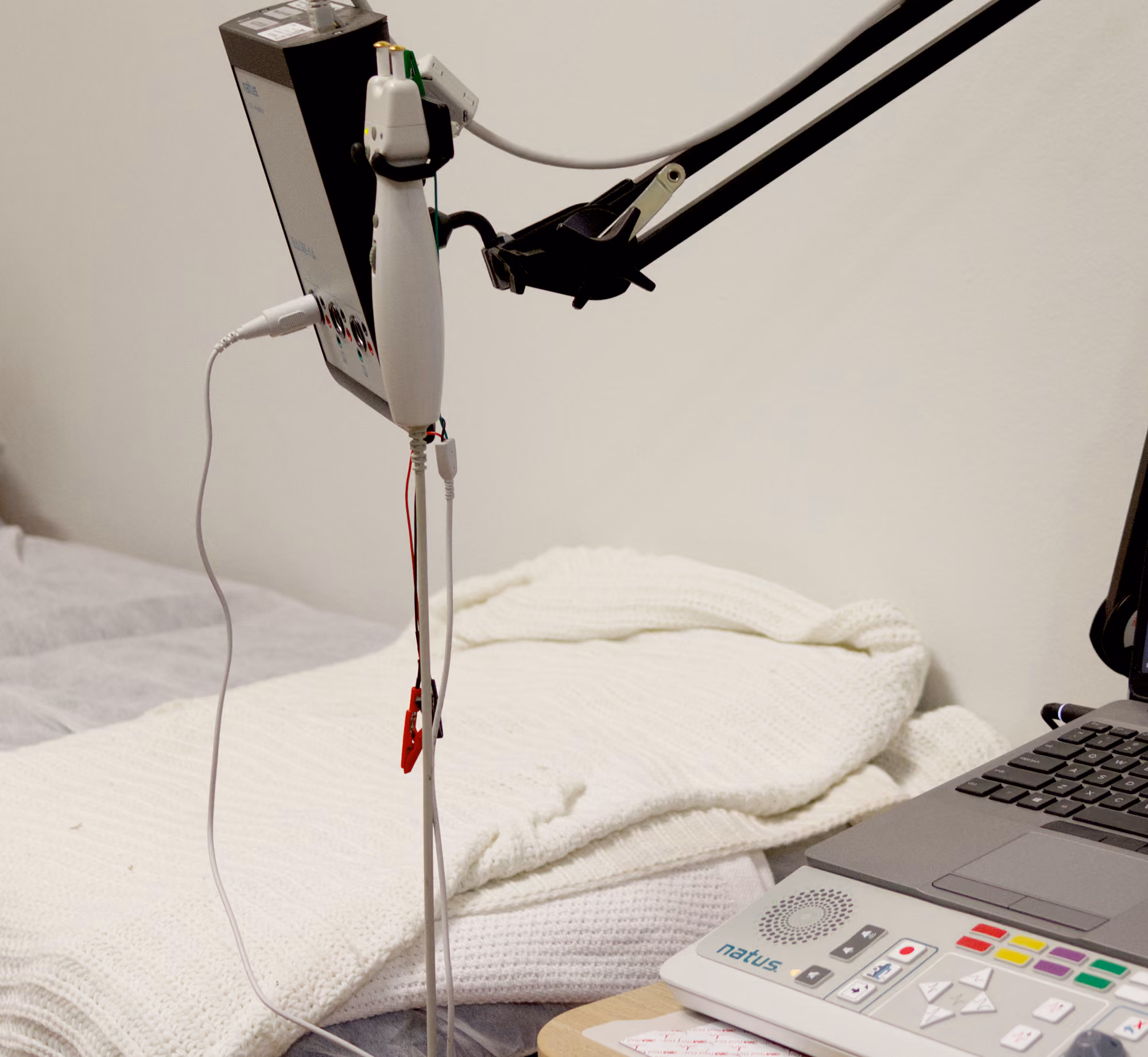 Neurophysiology testing device with handheld component and control panel on a bedside table.