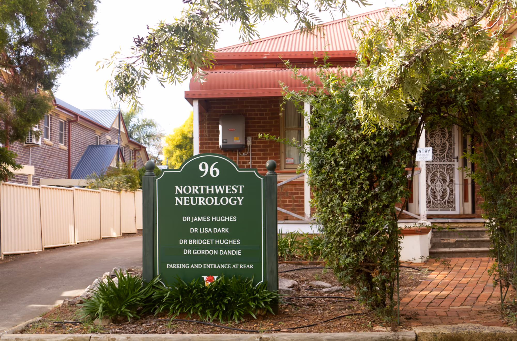 Green sign for Northwest Neurology at 96, listing four doctors, outside a brick building with red roof.