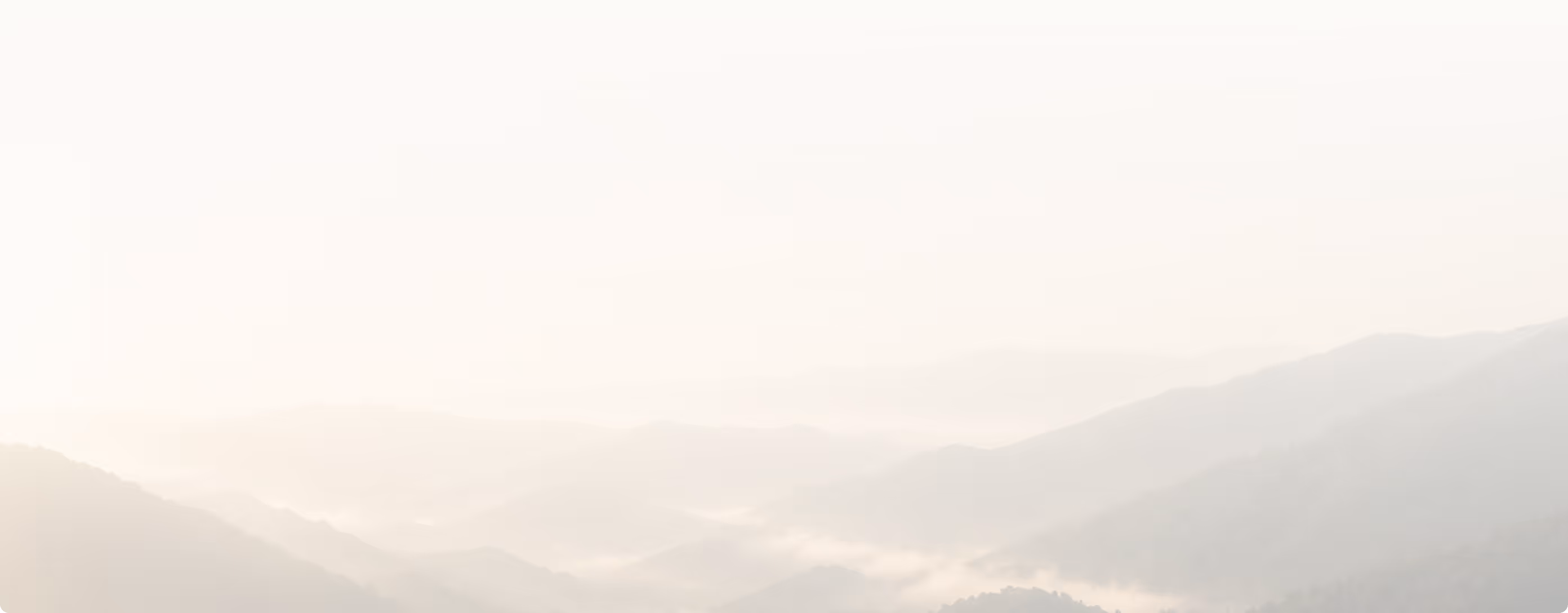 Softly lit mountain range with mist or fog settling in valleys under a pale sky.