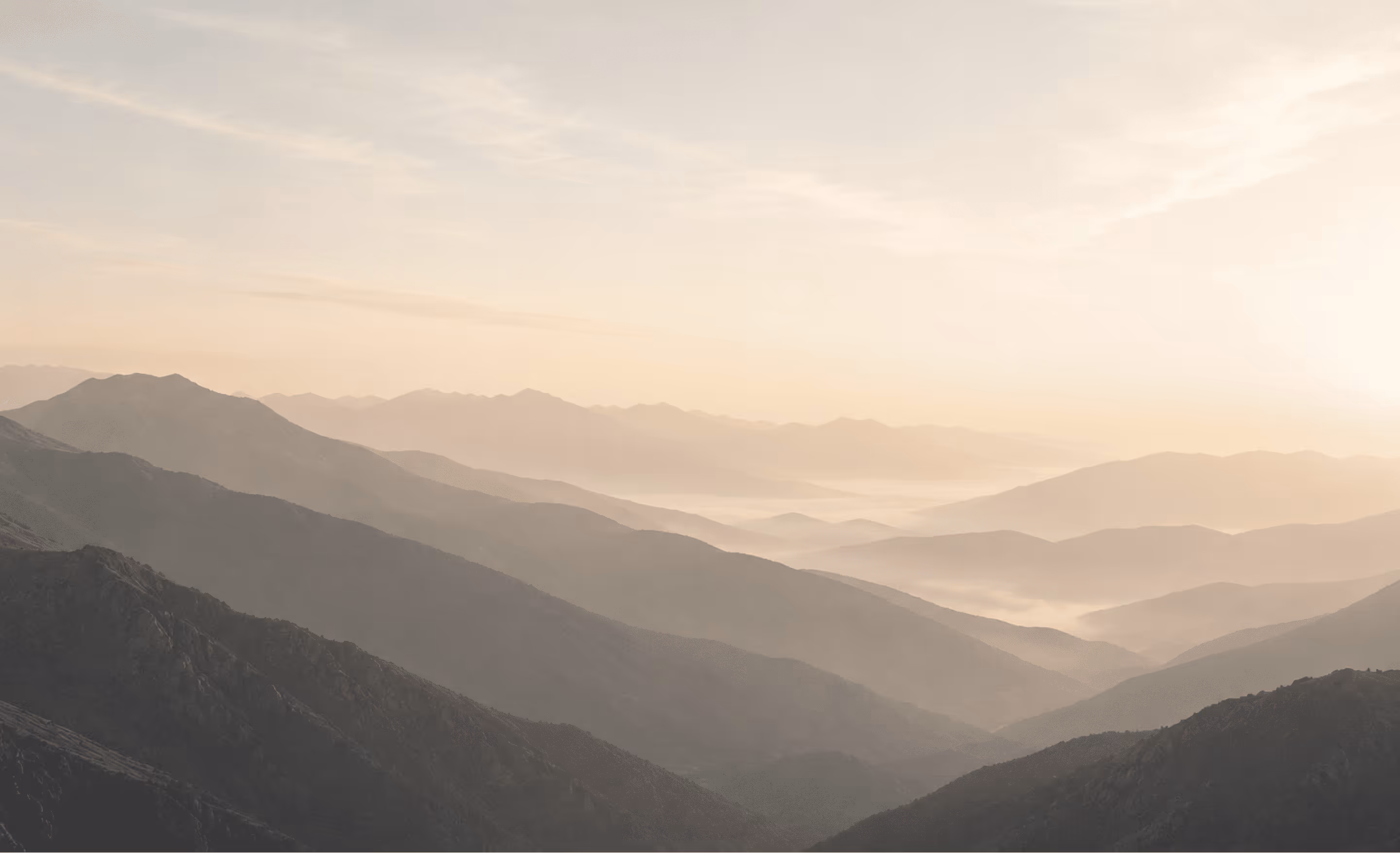 Layered mountain ranges fading into mist at sunrise with soft pastel sky.