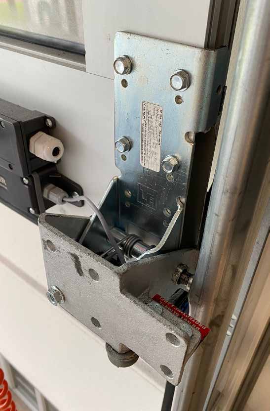 Nahaufnahme einer massiven metallenen Scharnierverbindung an einem Sektionaltor mit integrierter Feder und einem angeschlossenen elektronischen Sensor zur Sicherheitsüberwachung.