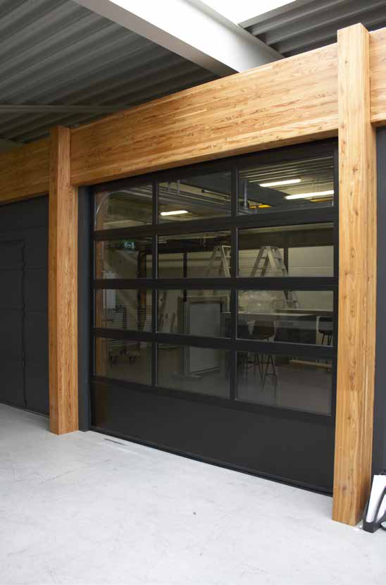 Zur Hälfte geöffnetes Sektionaltor in einer privaten Garage mit Blick nach draußen auf ein davor parkendes blaues Auto.