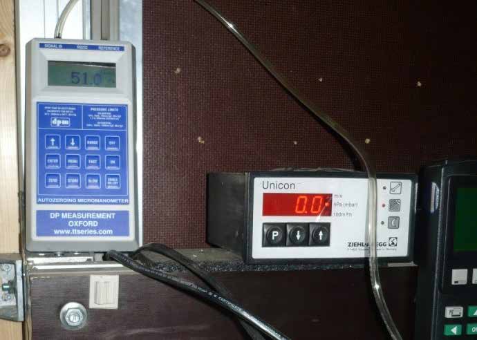Ansicht zweier elektronischer Messgeräte an einem industriellen Prüfaufbau. Auf der linken Seite ist ein blau-weißes "Autozeroing Micromanometer" der Marke DP Measurement angebracht, dessen Display den Wert 51.0 anzeigt. Rechts daneben steht ein "Unicon" Steuer- oder Anzeigegerät von Ziehl-Abegg mit einer leuchtend roten Digitalanzeige, die auf 0.0 steht. Die Geräte sind unter anderem mit transparenten Pneumatikschläuchen und schwarzen Kabeln verbunden.
