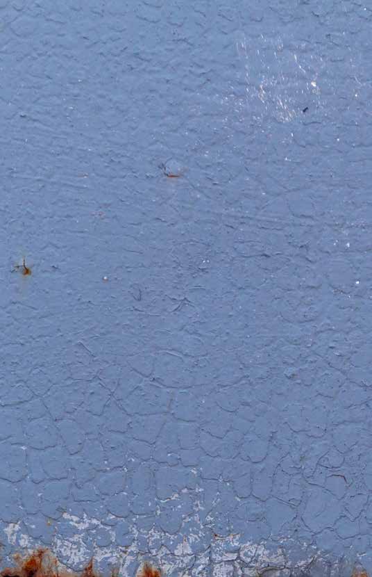 Nahaufnahme einer blauen, lackierten Oberfläche mit feinen Rissen im Lack und Roststellen am unteren Rand, was auf Alterung oder Witterungsschäden hinweist.