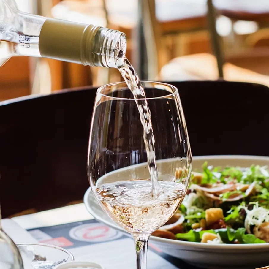Serveur qui sert du vin dans un verre à ballon avec un plat en arrière-plan
