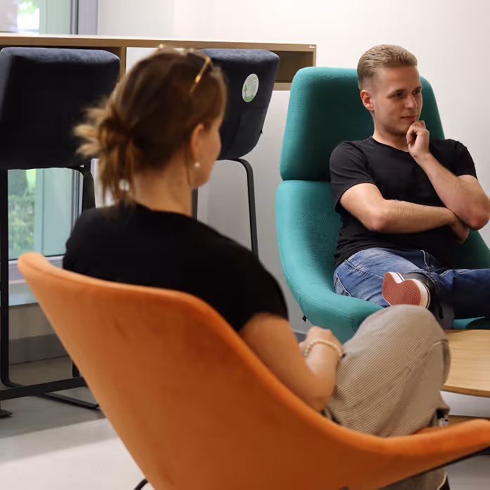 Two people sitting in modern chairs facing each other in a casual indoor setting.