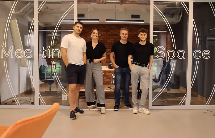 Four casually dressed people standing in front of a glass wall with 'Meeting Space' text.