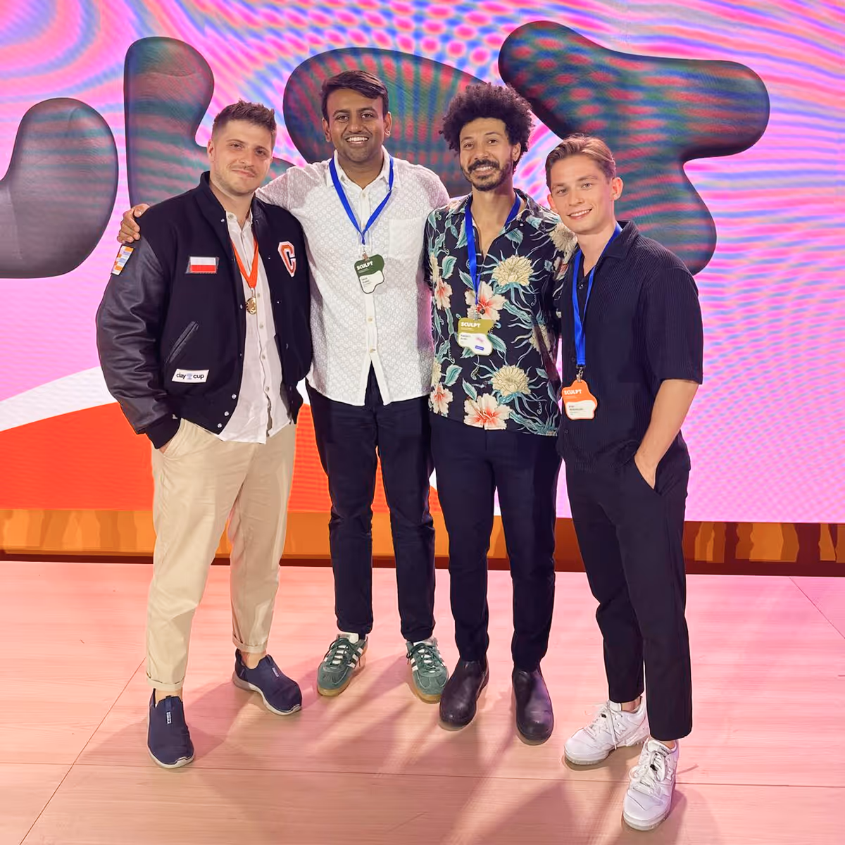 Four men with event badges stand smiling in front of a colorful abstract background.