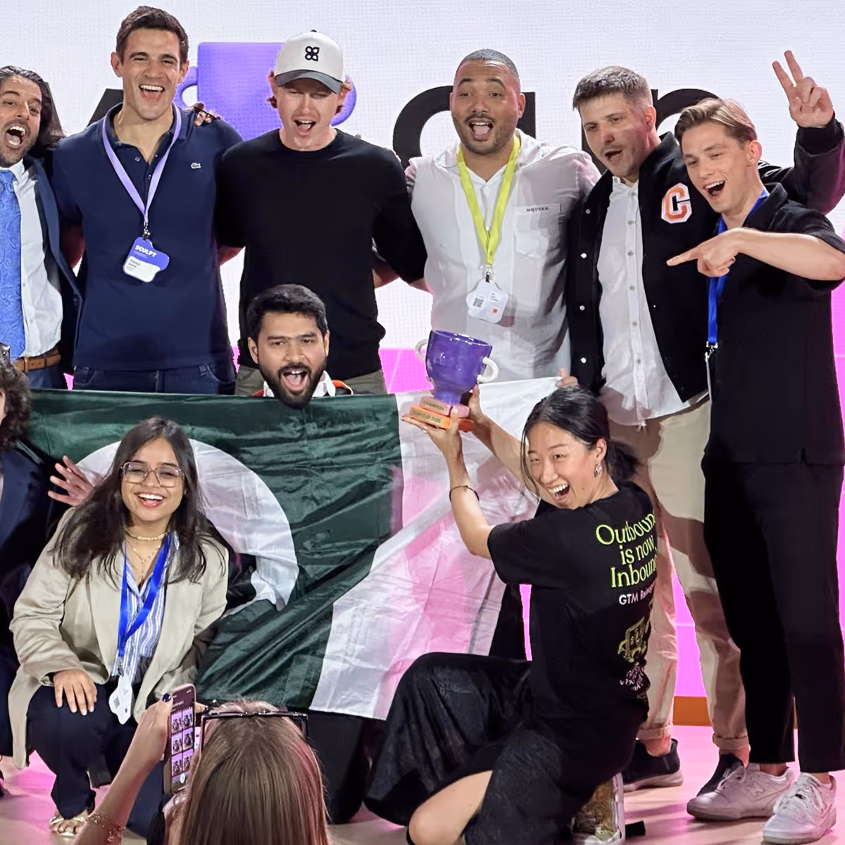 Group of diverse people celebrating with a trophy and a Pakistan flag, posing for a photo.