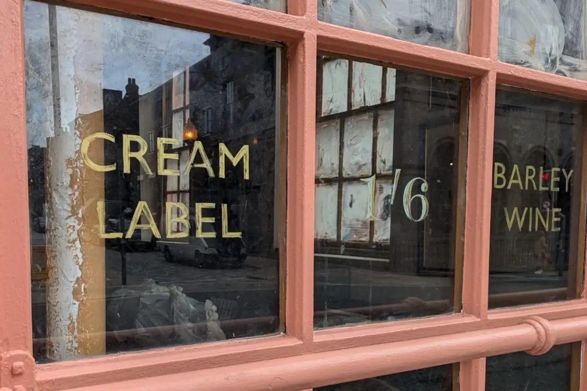 A close-up of a pub window with painted lettering reading “CREAM LABEL” and “BARLEY WINE.”