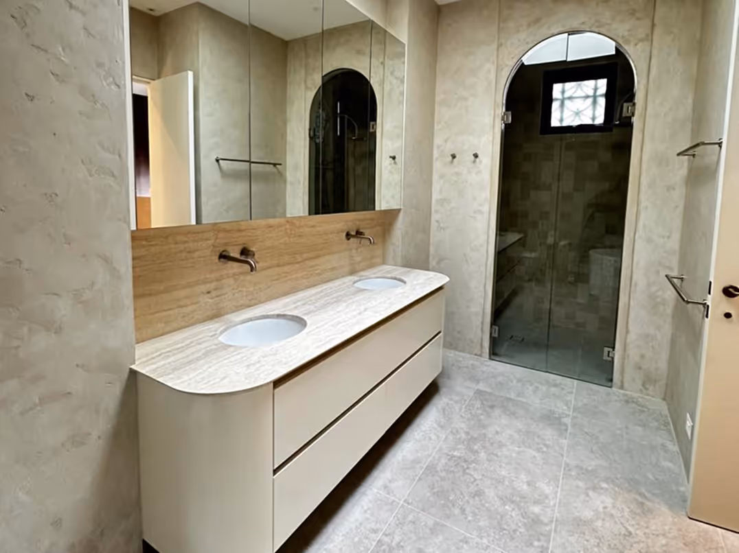 Modern bathroom with double sink vanity, large mirror, and glass door shower under arch.