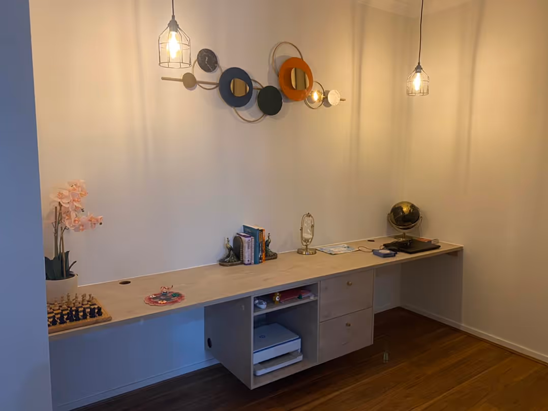 Long wooden desk with books, globe, orchid, chess set, and pendant lights in a minimalist room.
