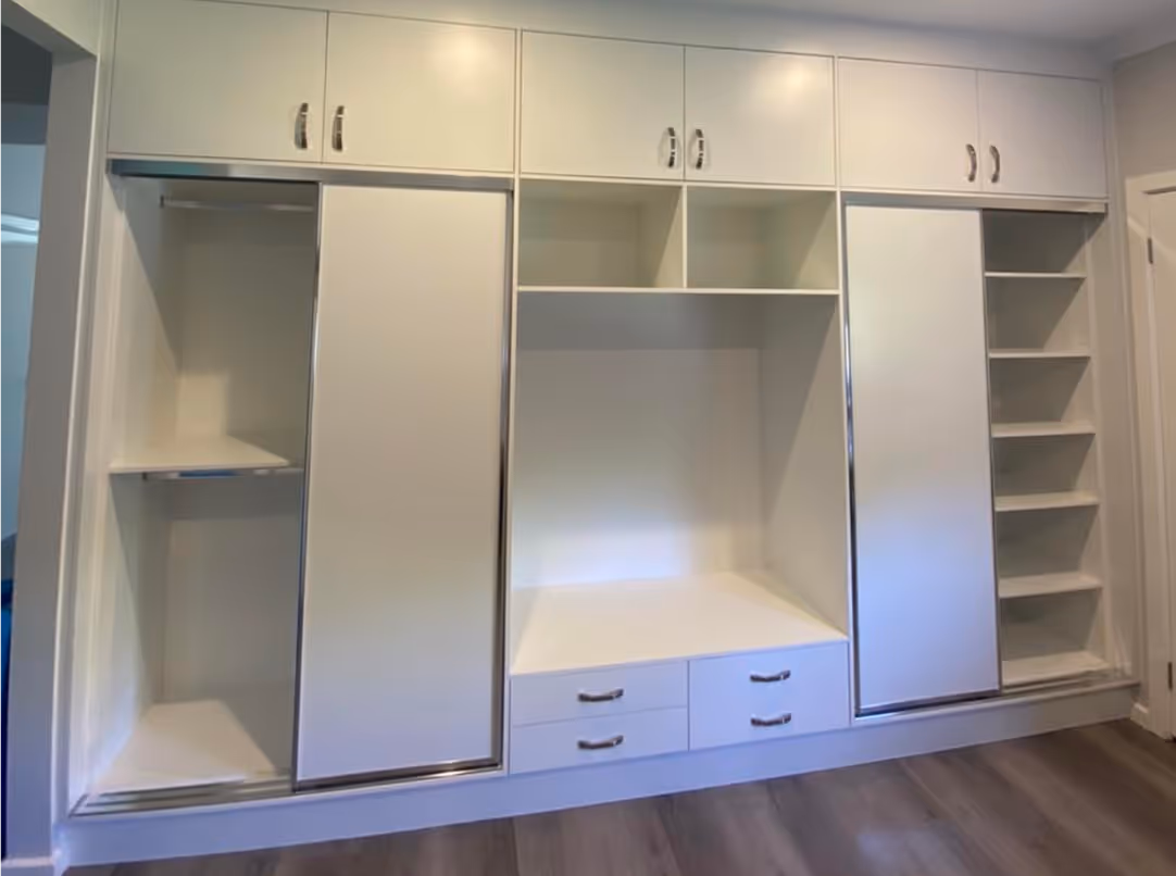 White built-in wardrobe with sliding doors, shelves, and drawers in a room with wood flooring.