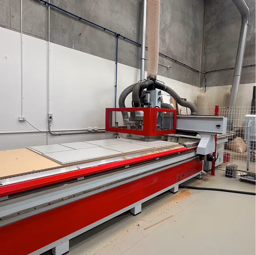 Industrial CNC machine with red frame and multiple hoses inside a clean factory space.