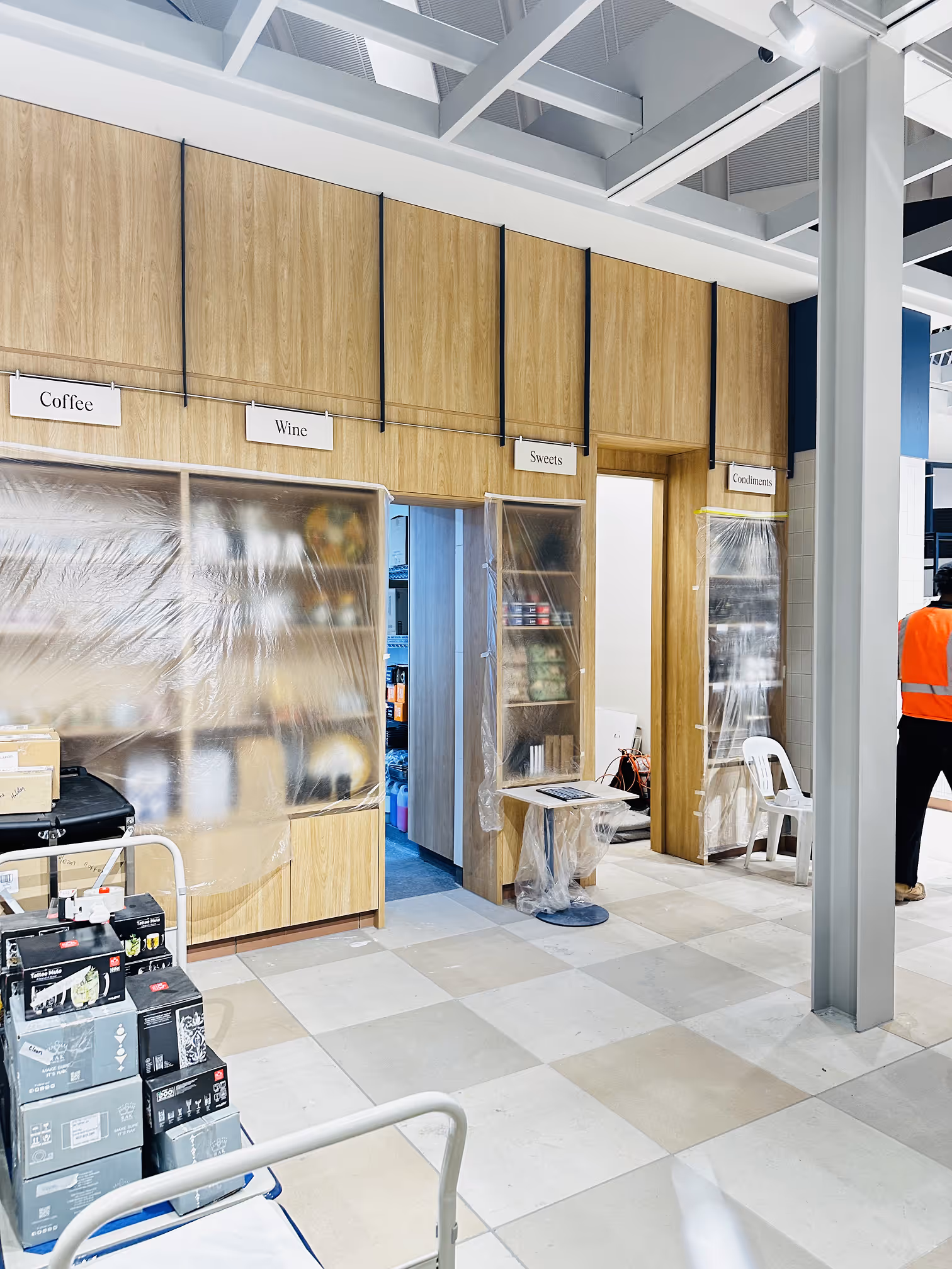 Indoor storage area with labeled sections: Coffee, Wine, Sweets, and Condiments covered with plastic sheets.