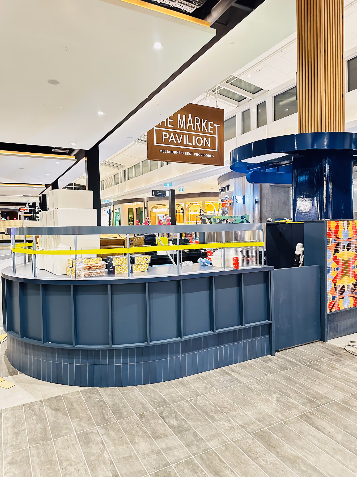 Empty modern market stall counter with boxes and a sign reading The Market Pavilion in a shopping mall.
