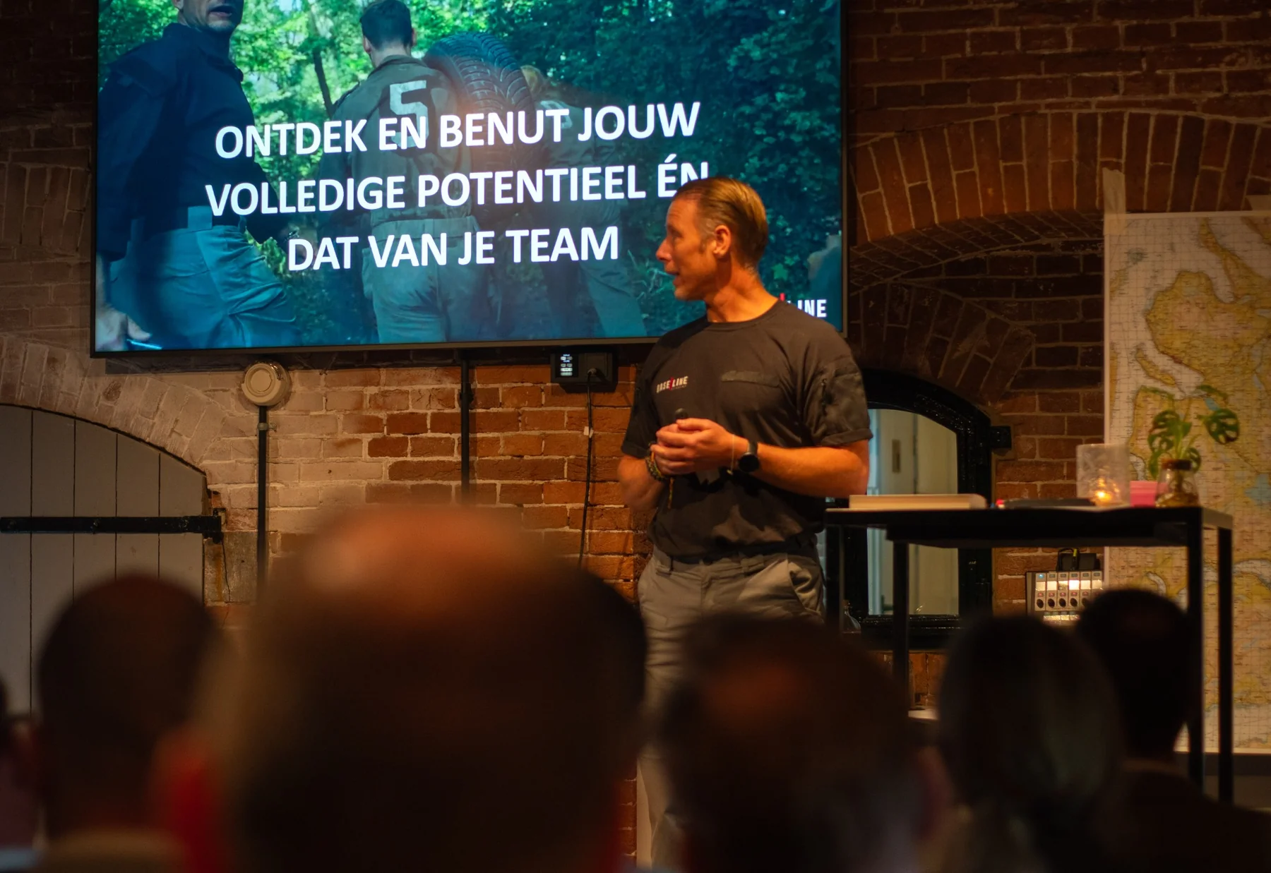 Man geeft een presentatie aan een kleine groep mensen tegen een muur met neonlichtlijnen.