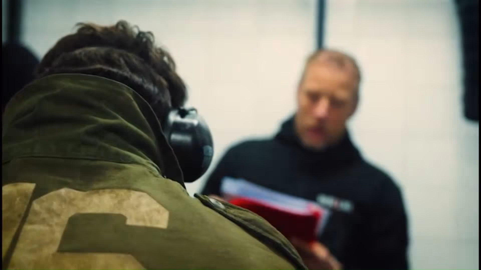 Man met donkere jas staat buiten in het donker, kijkt naar rechts met handpalmen samen.