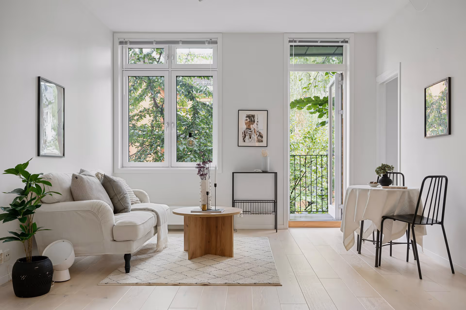 Minimalist living room with white sofa, wooden table, indoor plants, and glass door opening to greenery.
