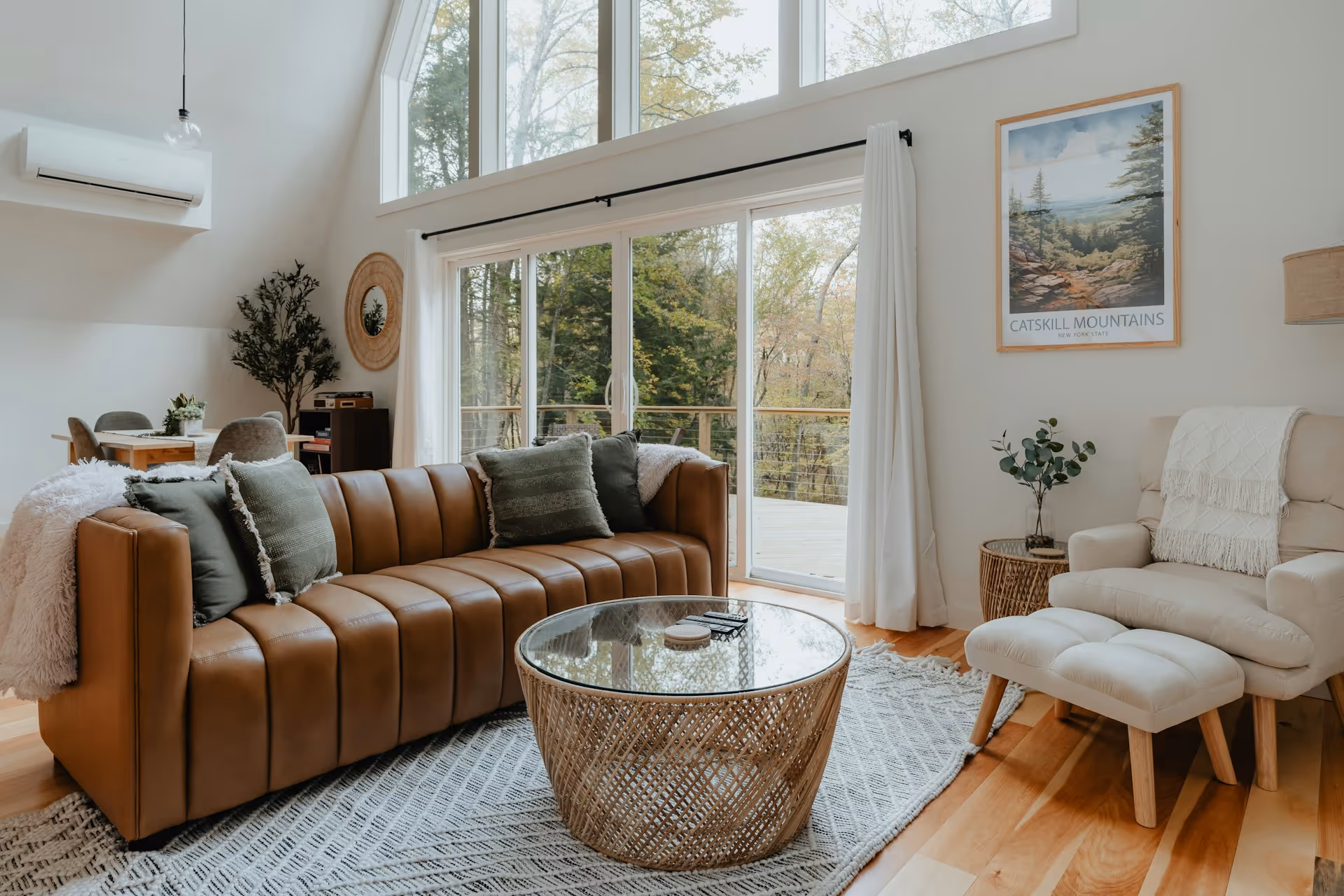 Cozy living room with brown leather sofa, glass coffee table, cream armchair, and large windows.