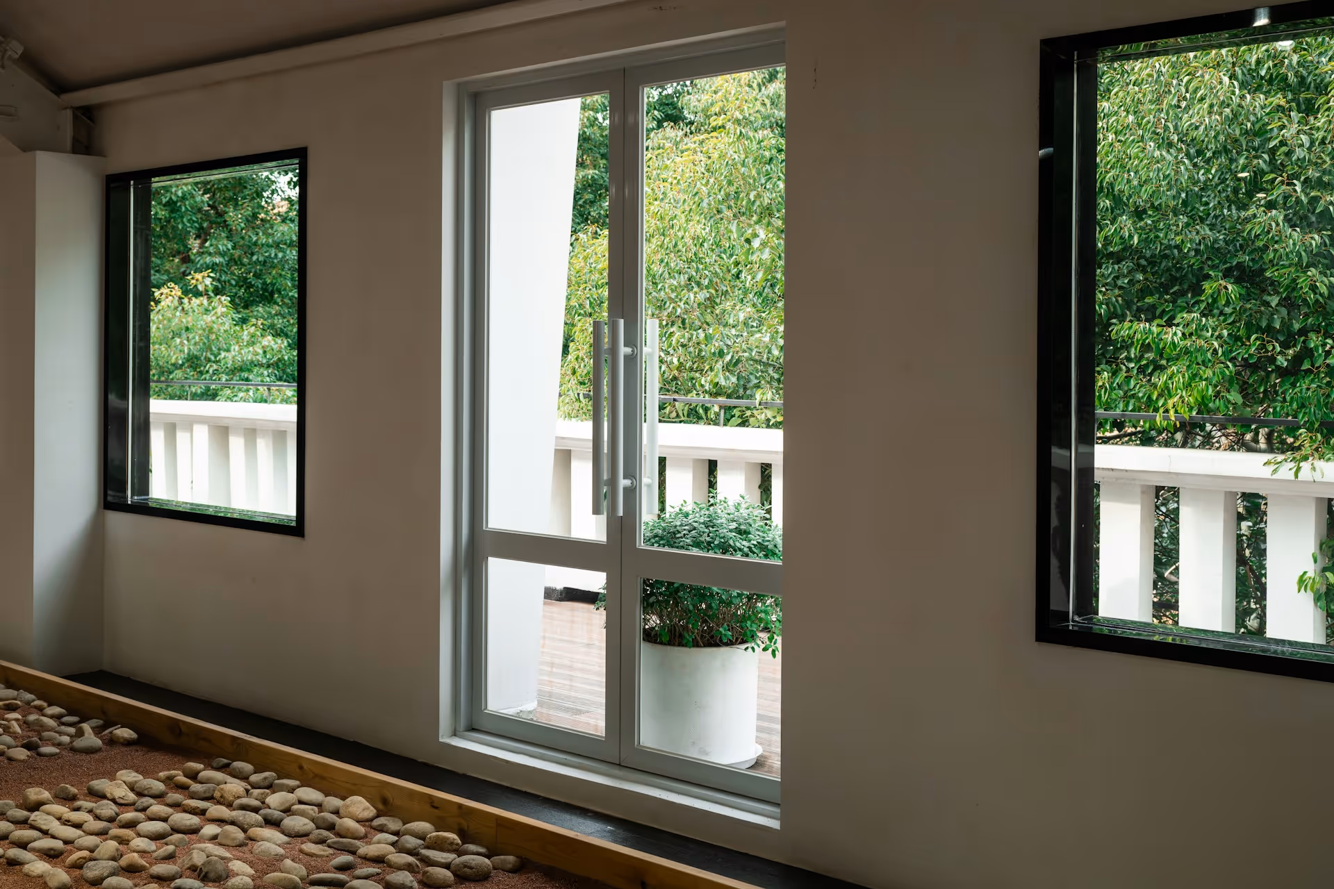 White glass door between two windows with green trees and a plant in a white pot outside.