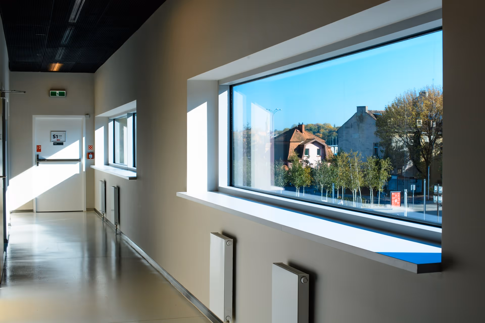 Bright hallway with large window showing houses and trees outside on a sunny day.