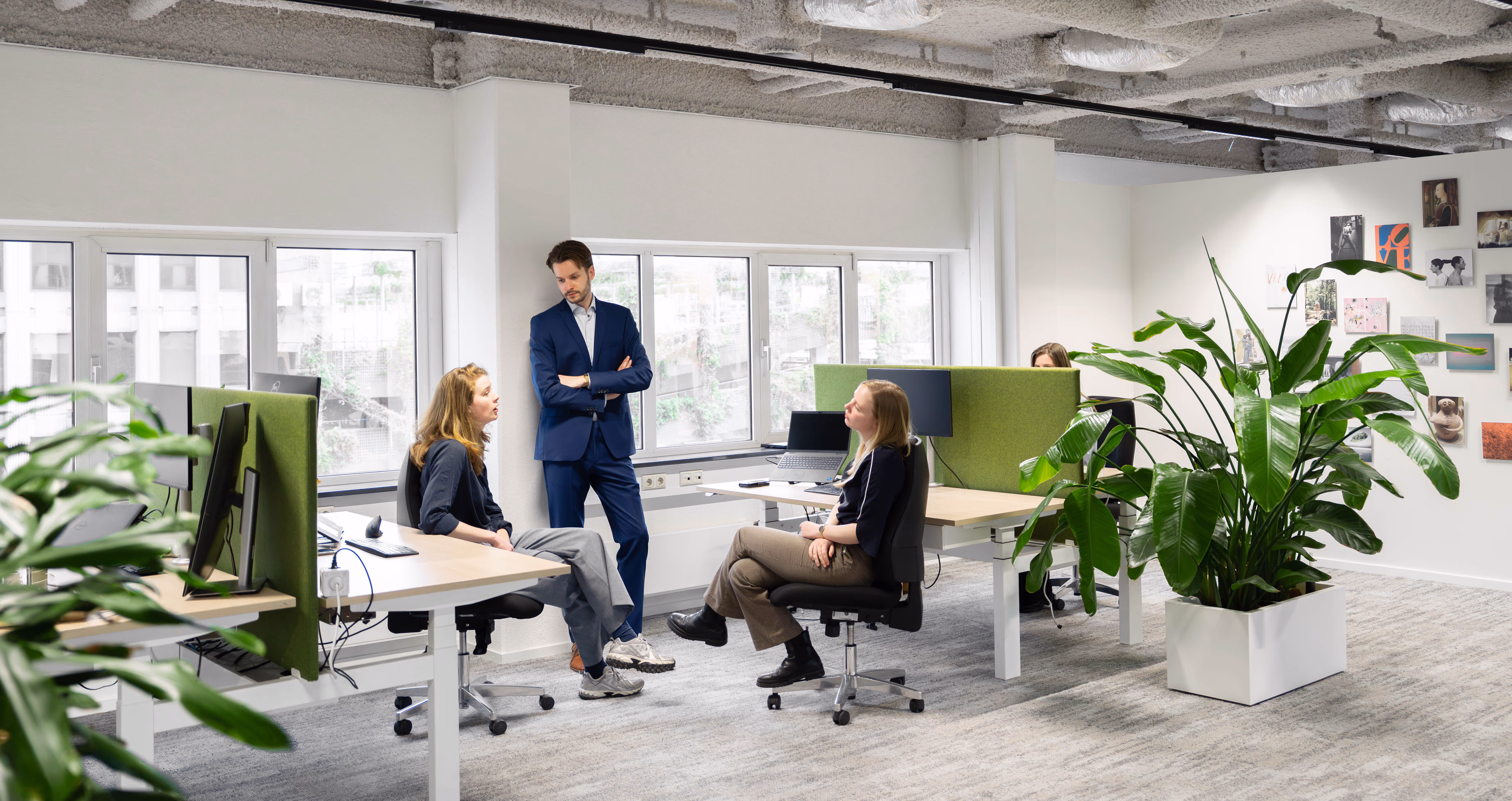 Drie collega's praten in een moderne kantoorruimte met groene planten en bureaus.