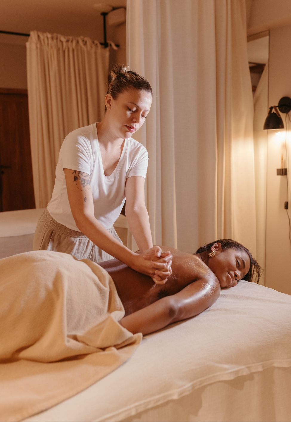 Woman giving a back massage to a relaxed client lying face down covered by a beige towel.