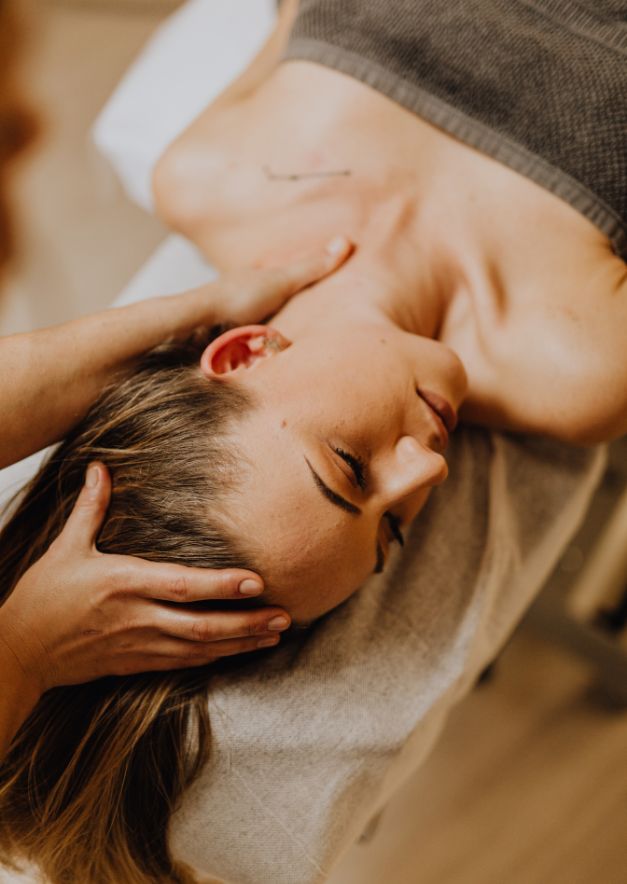 Woman receiving a relaxing head and neck massage while lying on a massage table with eyes closed.