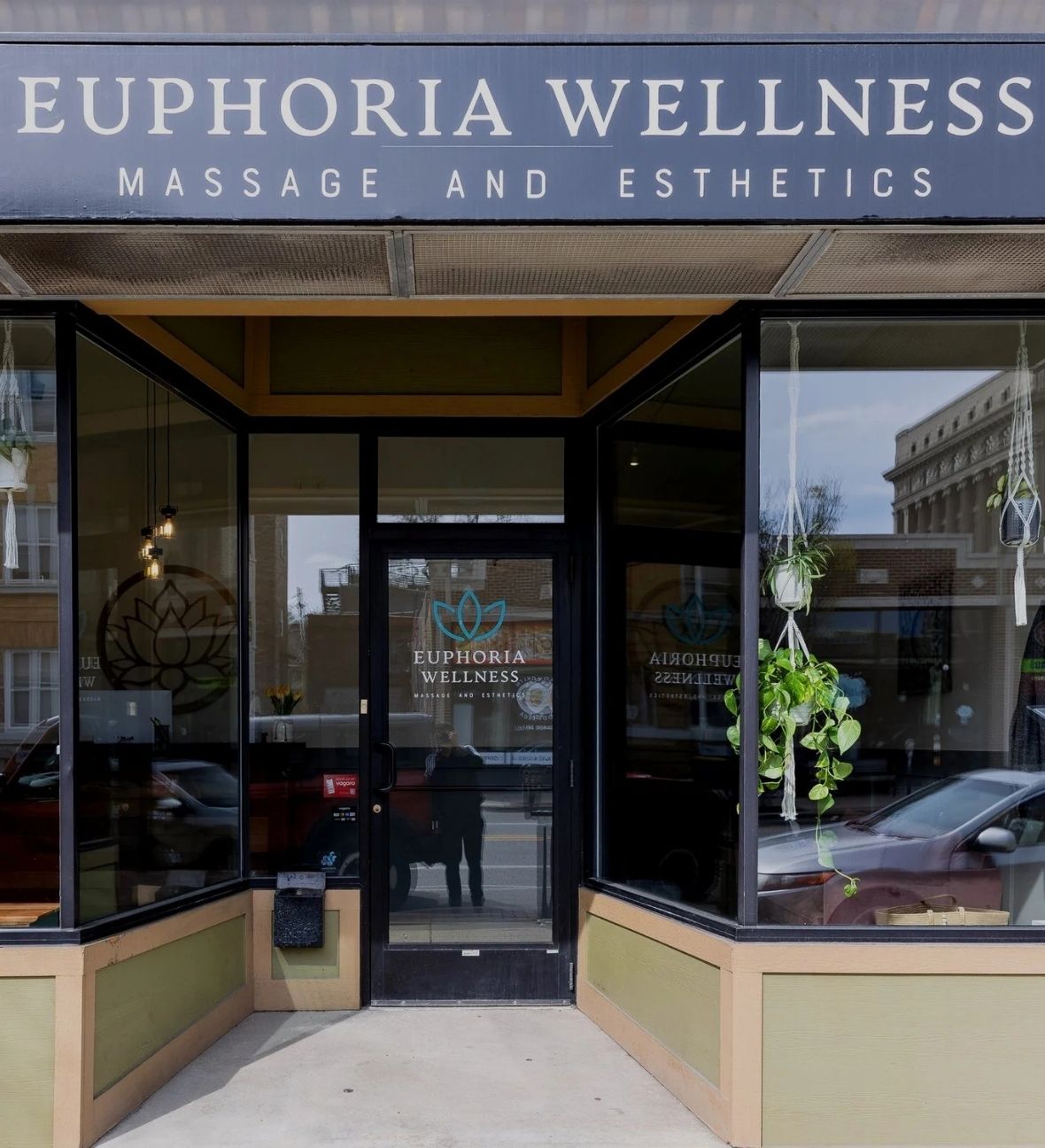 Storefront of Euphoria Wellness offering massage and esthetics with hanging plants in windows.