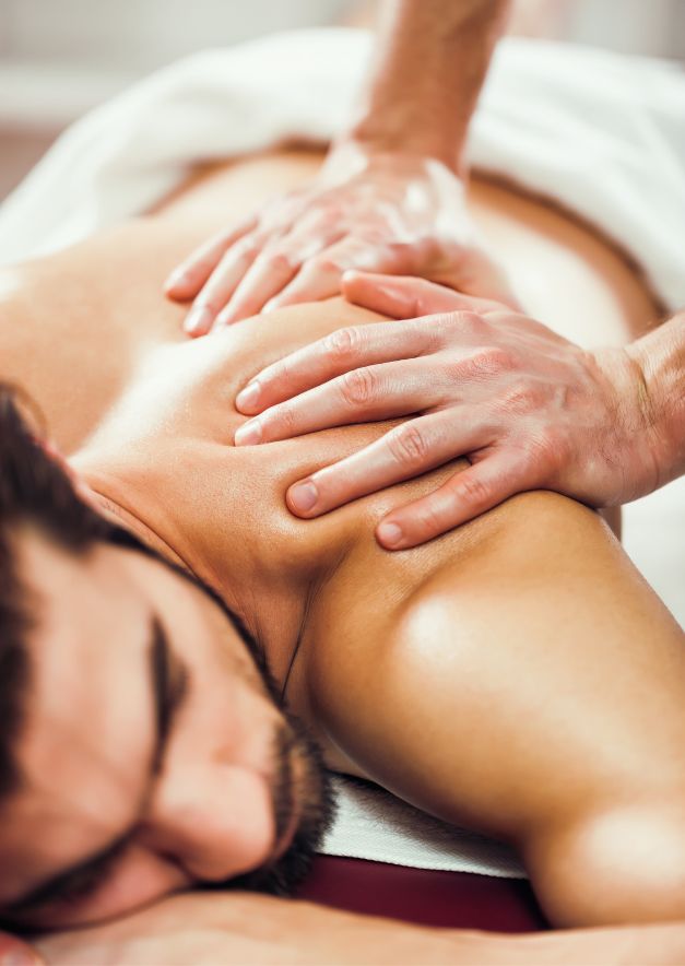 Man lying face down receiving a back massage with hands pressing on his shoulder blades.