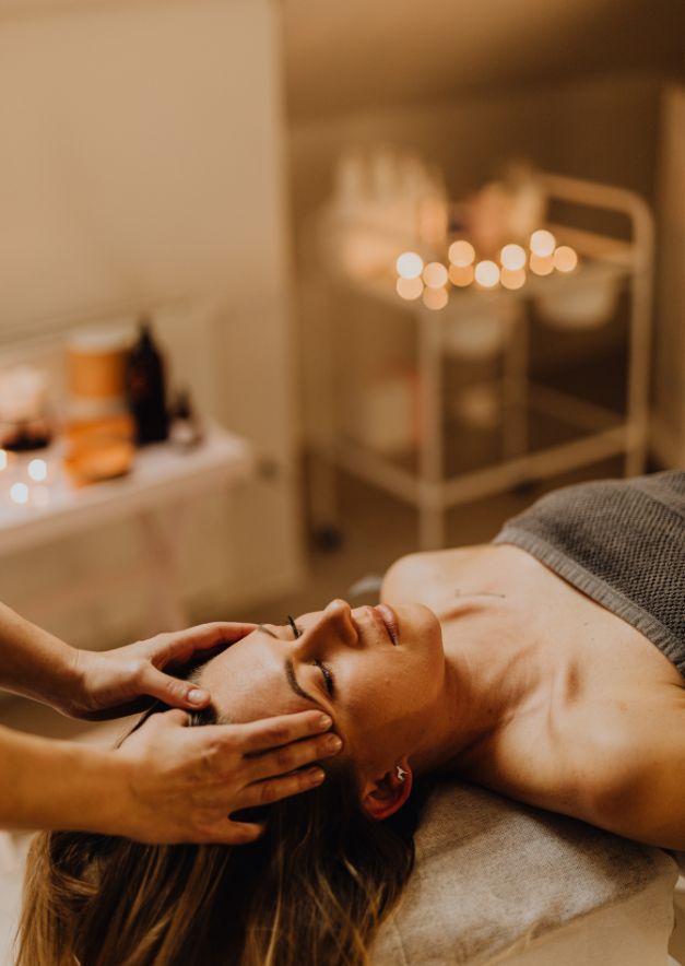 Woman lying on spa table receiving a relaxing face massage in a softly lit treatment room.