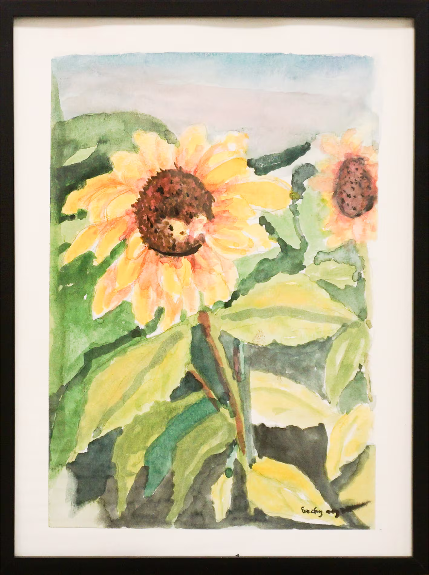 A watercolor painting of two sunflowers with green leaves in a black frame.