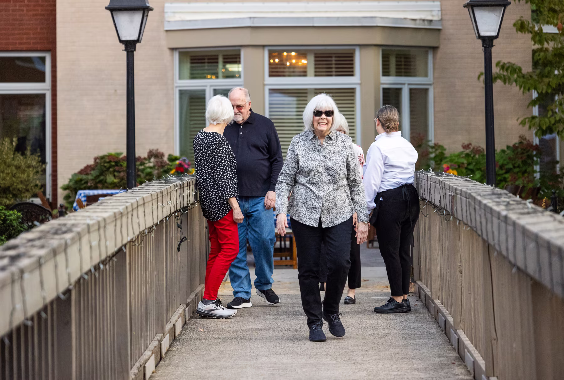 Four people walk across a bridge, socializing and smiling in a friendly setting.
