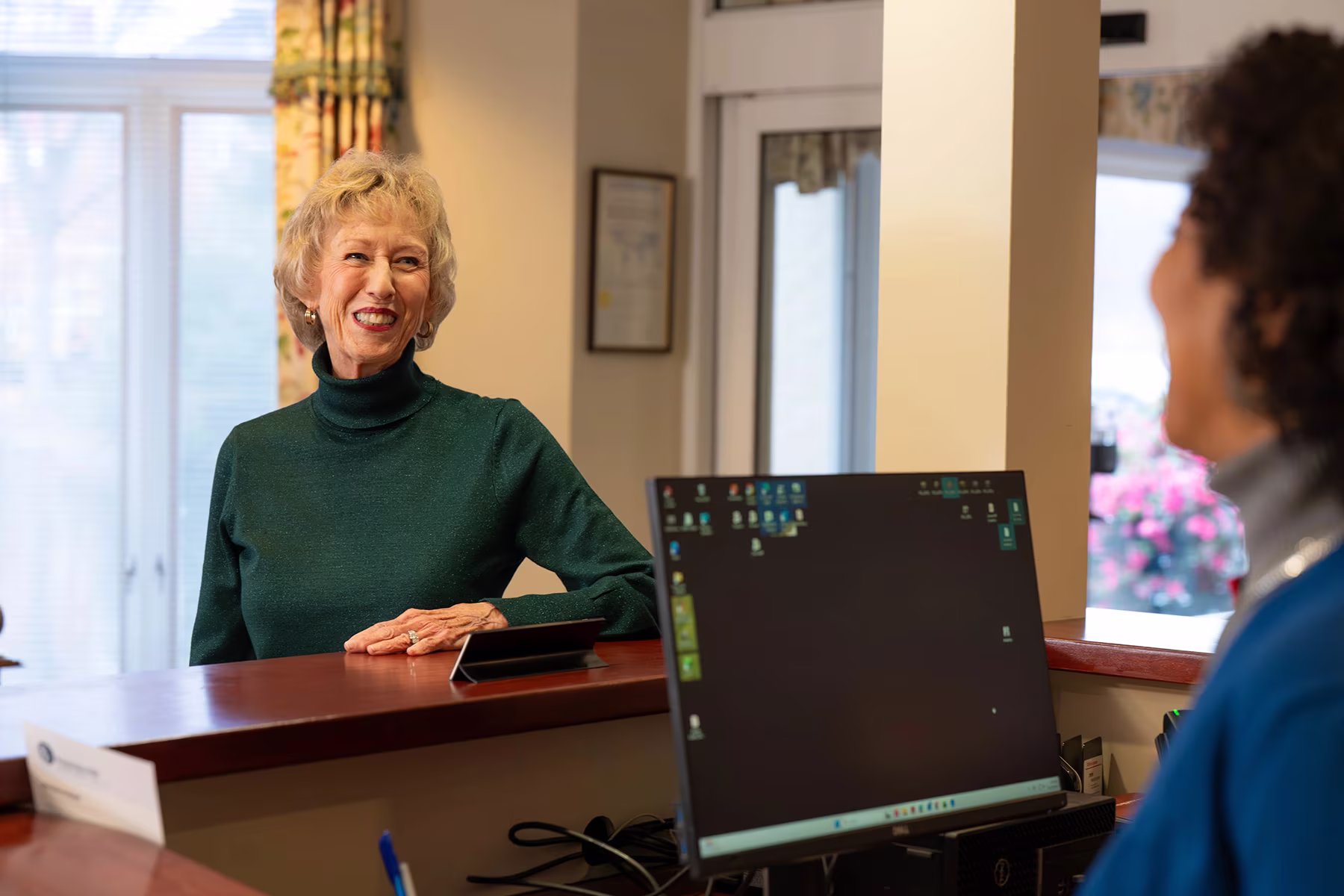 A woman at a reception counter smiles while talking to another person.