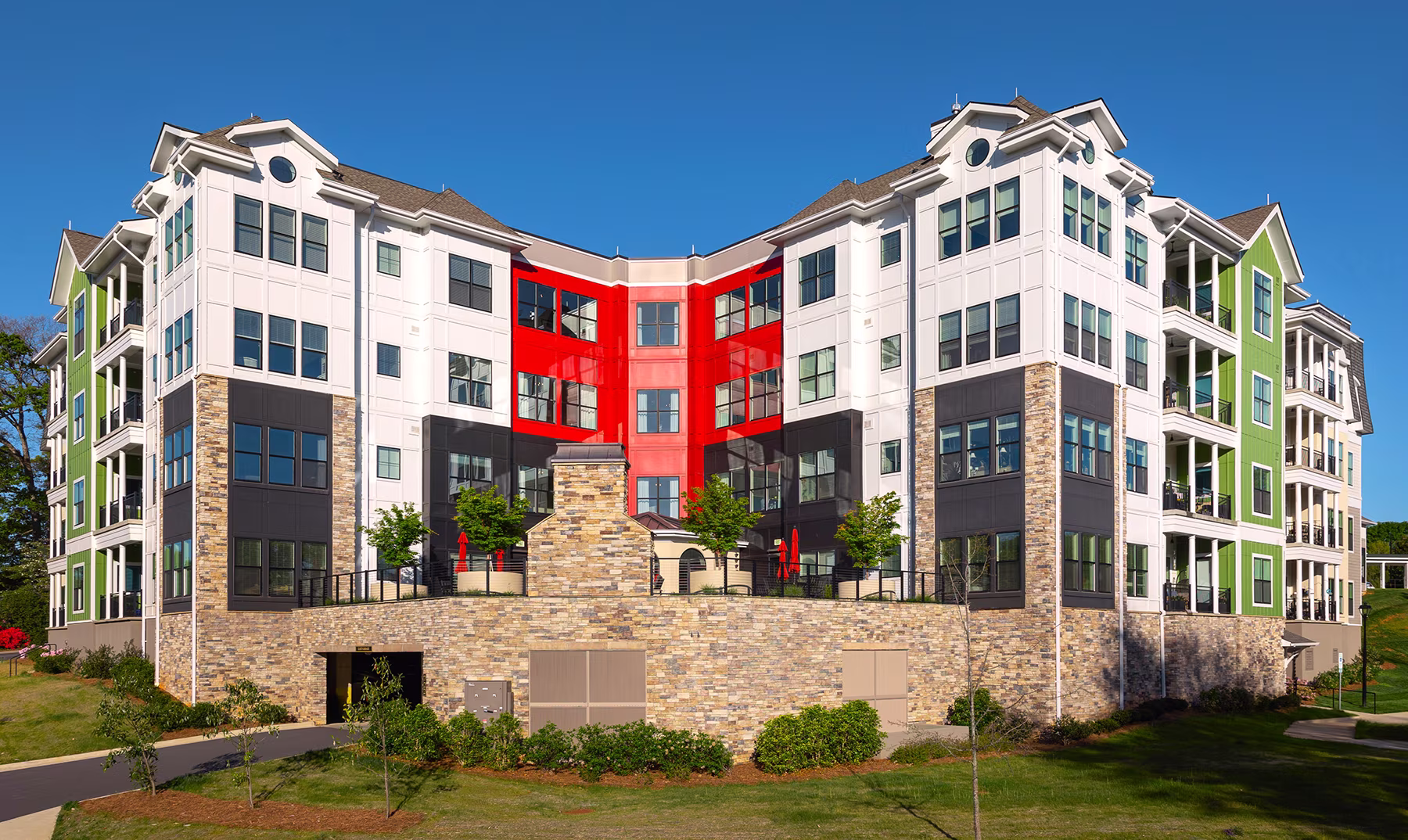 A modern, multi-story apartment building with colorful sections and a stone facade under a clear blue sky.