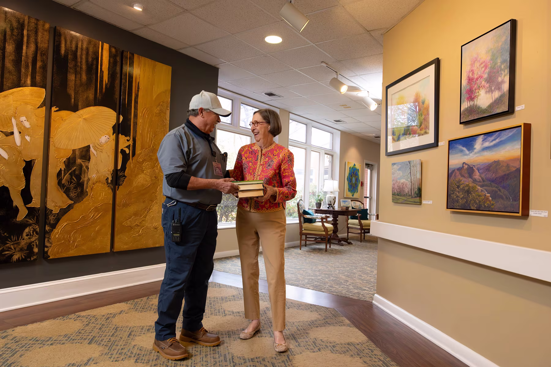 A man hands a book to a smiling woman in an art gallery setting.