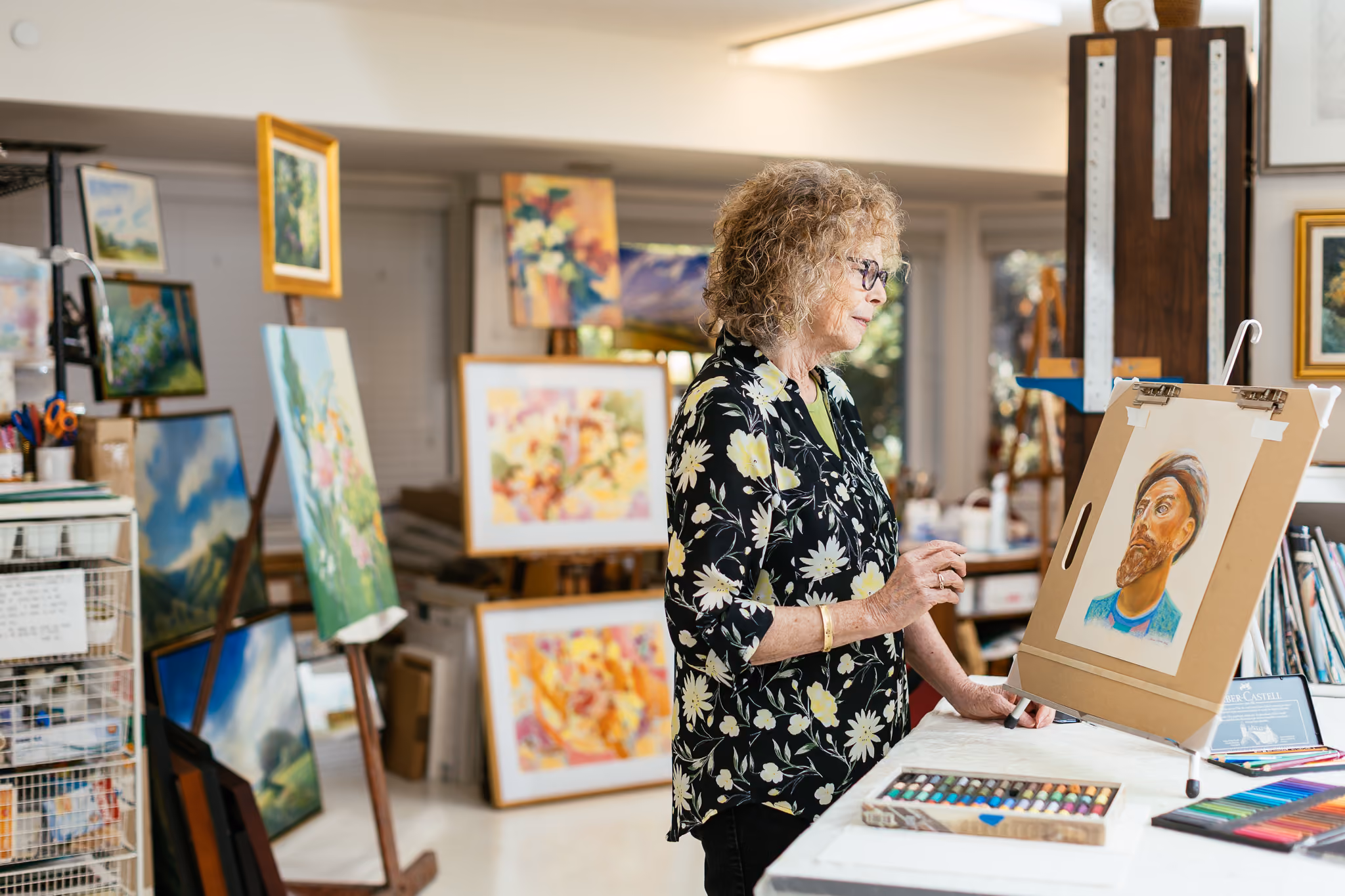 Person painting a portrait in an art studio filled with colorful paintings and art supplies.