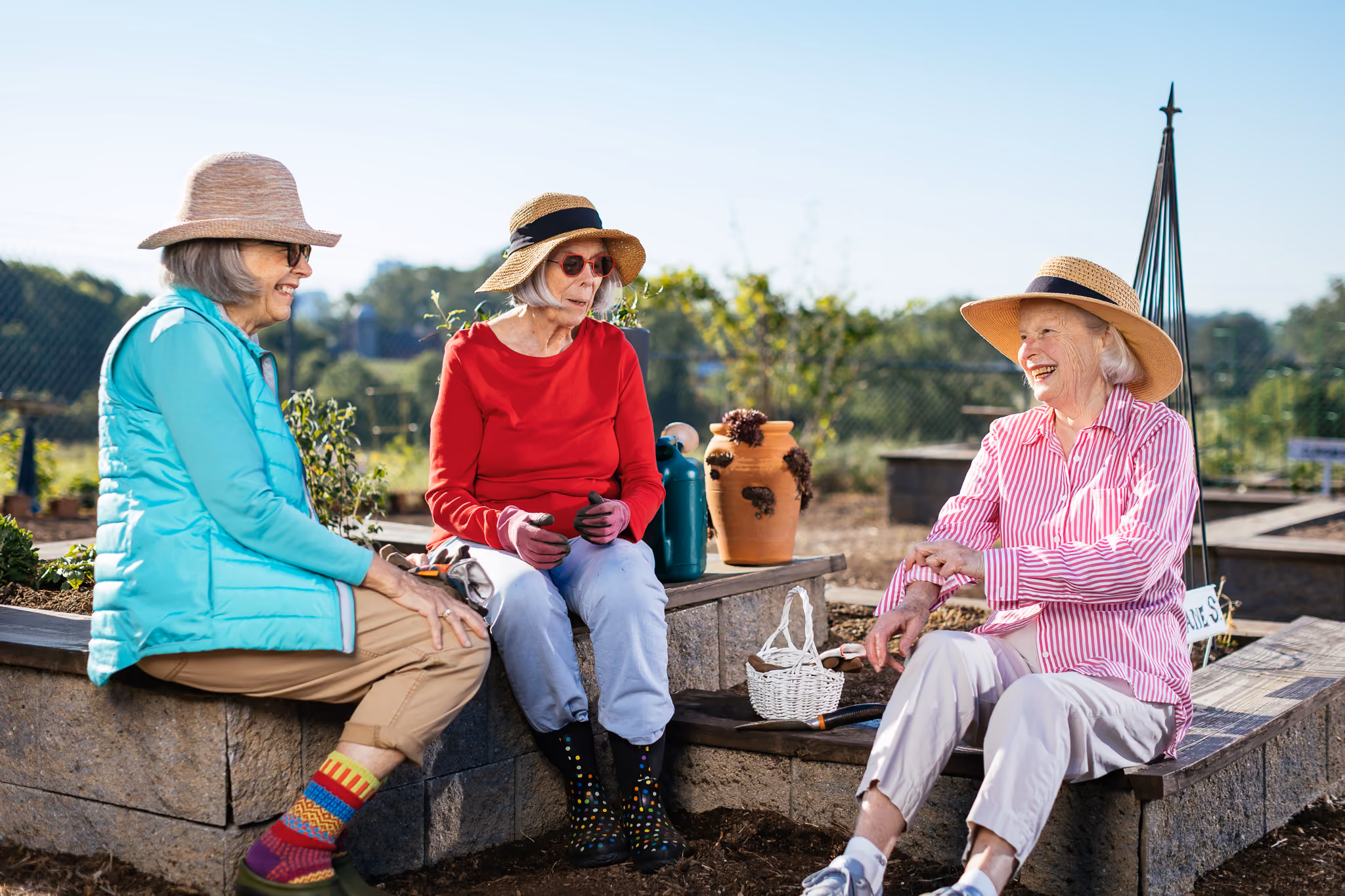 Three women wearing sun hats sit and chat cheerfully in a garden.