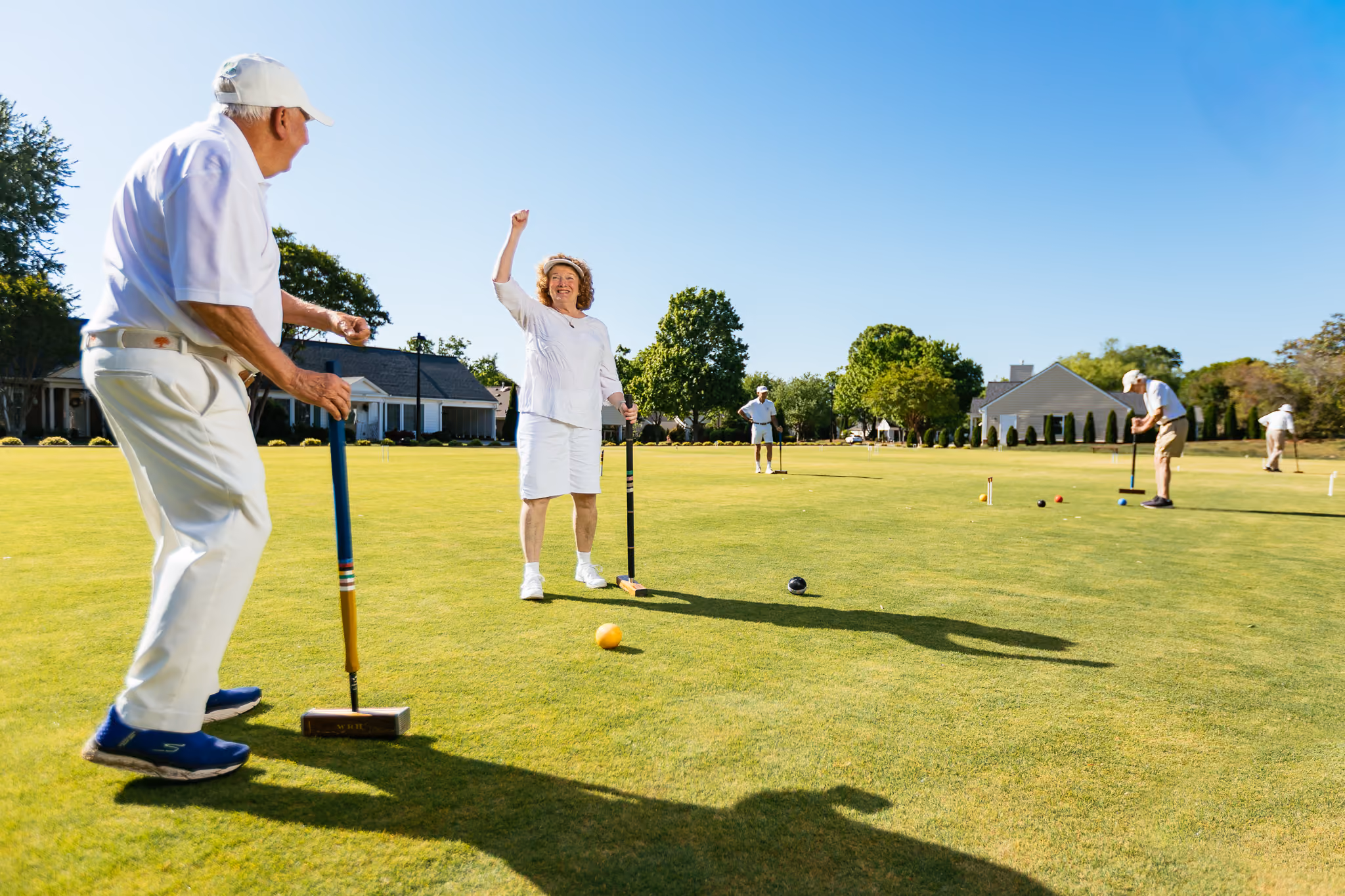 People playing croquet on a sunny day, one person raises their arm in celebration.