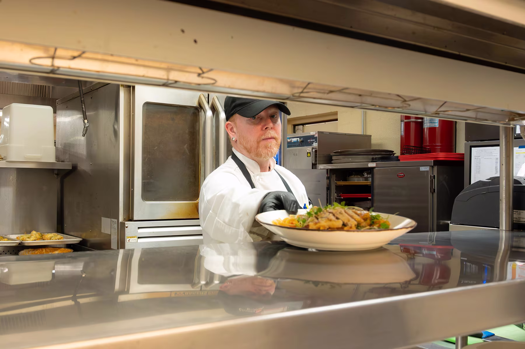 A chef places a plated meal on a stainless steel counter in a restaurant kitchen.
