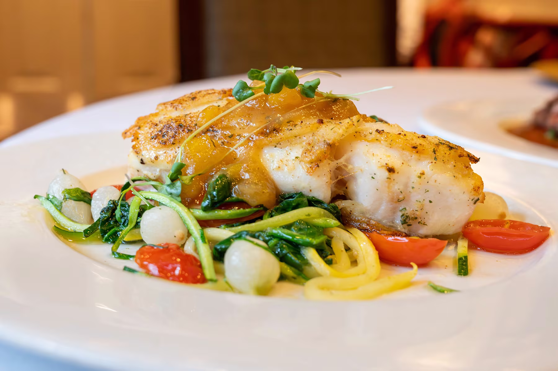 Grilled chicken breast with sauce on a bed of vegetables and garnished with greens on a plate.