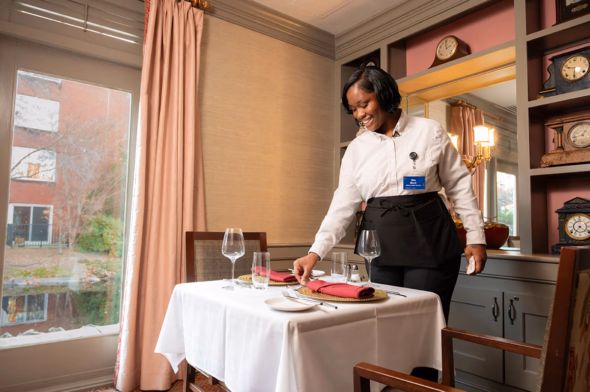 A server arranges a table setting in a restaurant, preparing for guests' arrival.