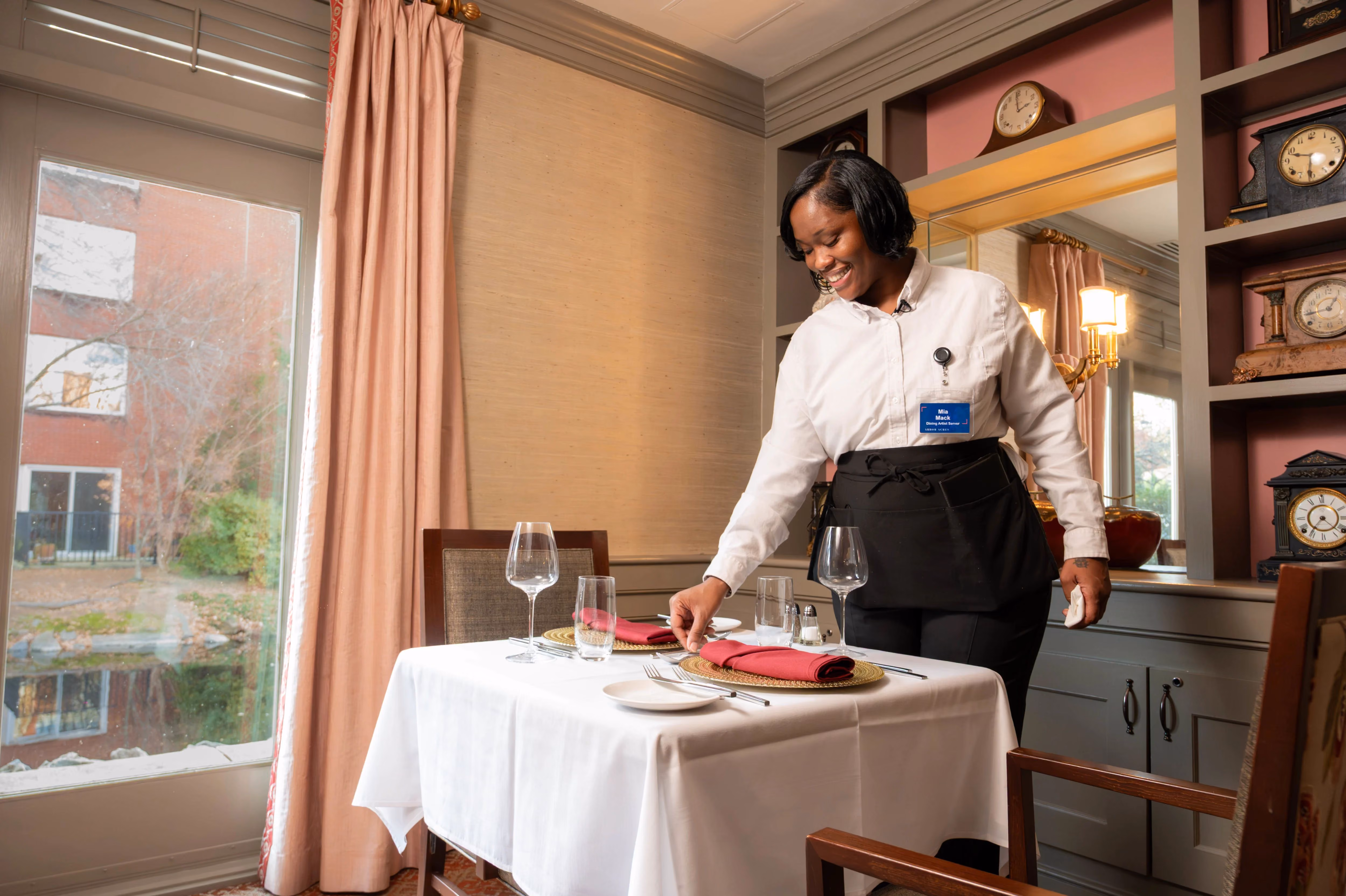A server arranges a table setting in a restaurant, preparing for guests' arrival.