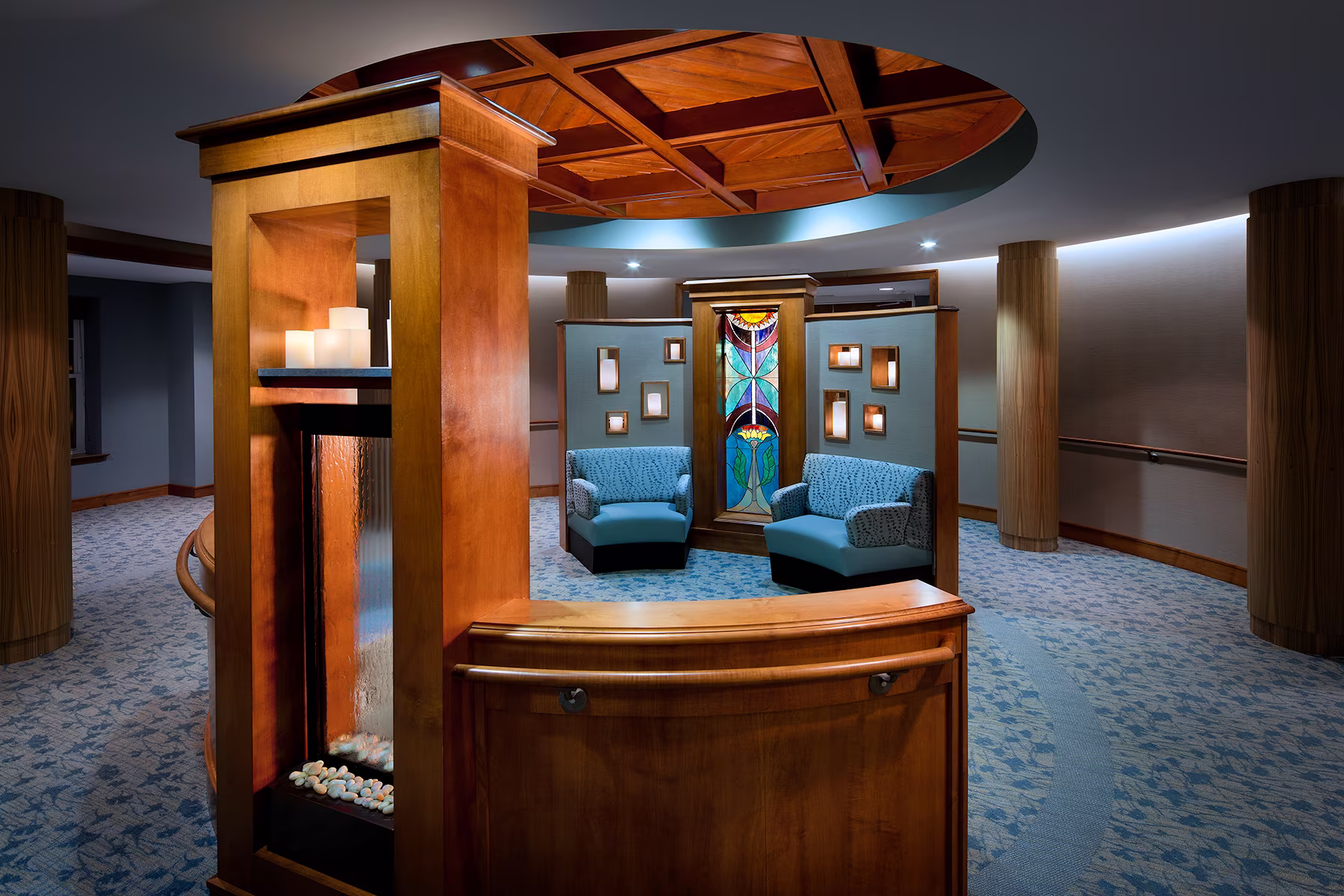 Two blue armchairs face a decorative stained glass panel in a warmly lit room with wooden accents.